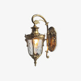 Gold outdoor wall light, an ornate lantern with water glass hanging from a scrolled arm