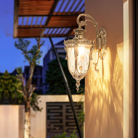 The lantern lit on a white wall beside a pergola and a gate at dusk