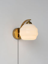 The gold sconce with a beige globe lit softly, the cord hanging straight