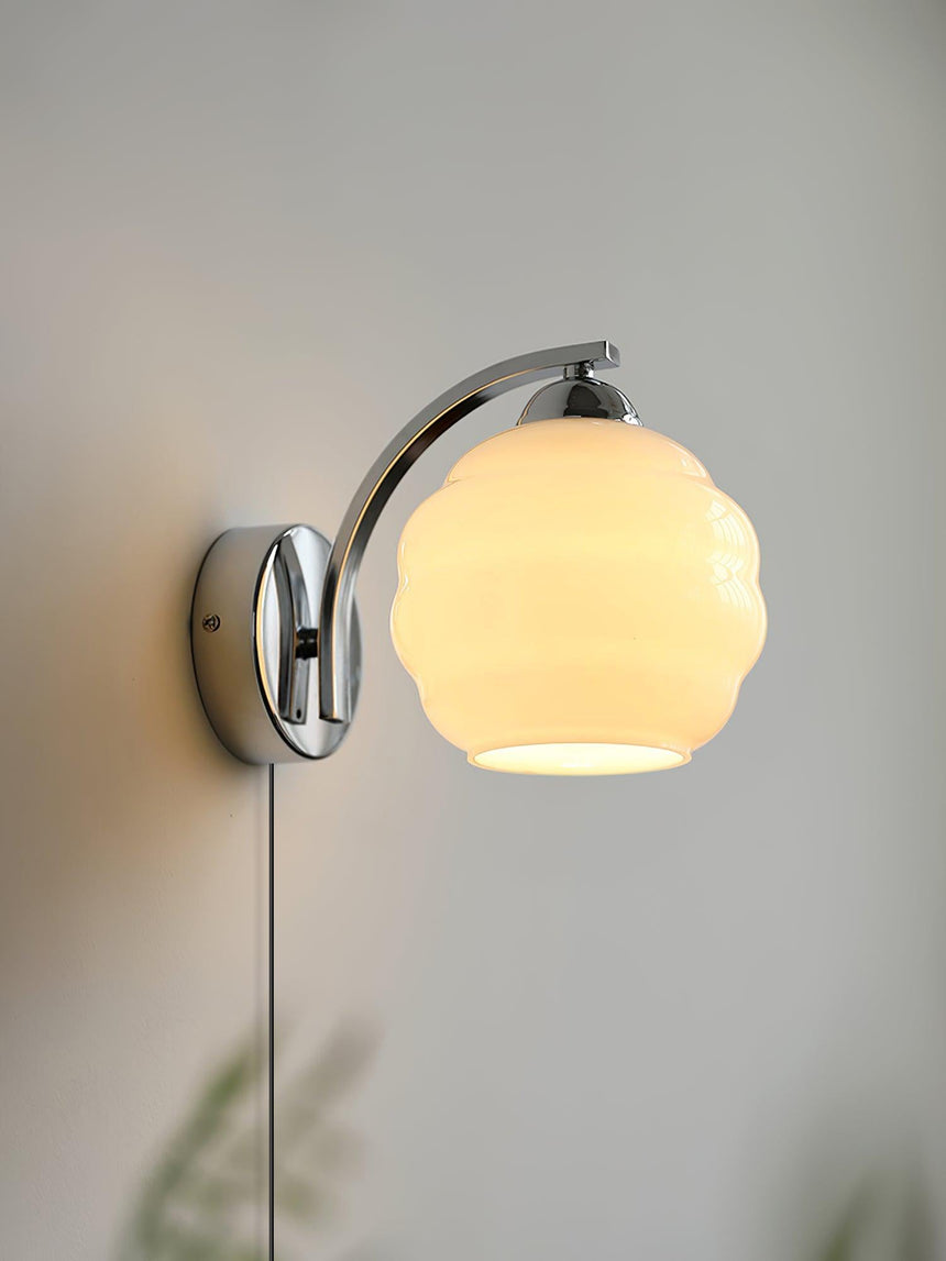 The chrome plug-in sconce lit on a gray wall, the cord running down