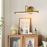 Gold bar lit above framed prints and a pleated lamp on a fluted wood cabinet