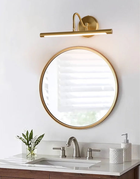 Gold bar lit above a round mirror over a stone basin with a plant and a bottle