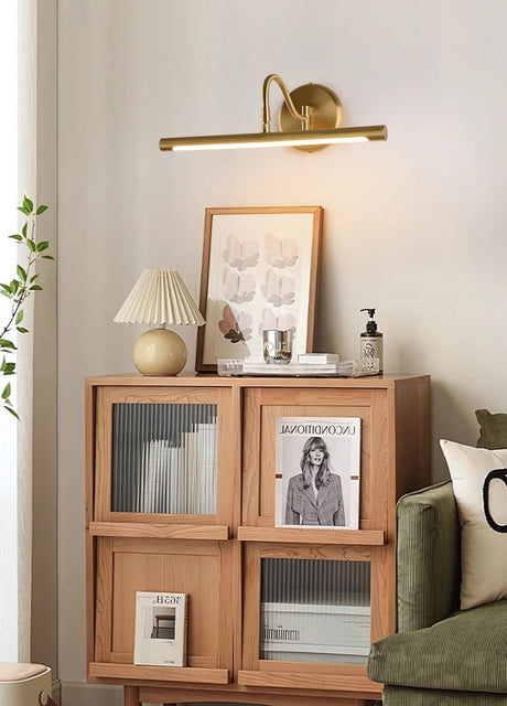 Gold bar lit above a wood shelf unit of framed prints beside a green sofa