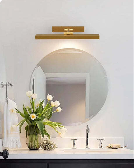 Gold bar above a round bathroom mirror with tulips on the counter