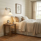 The sconce lit above a nightstand beside a bed with plaid pillows