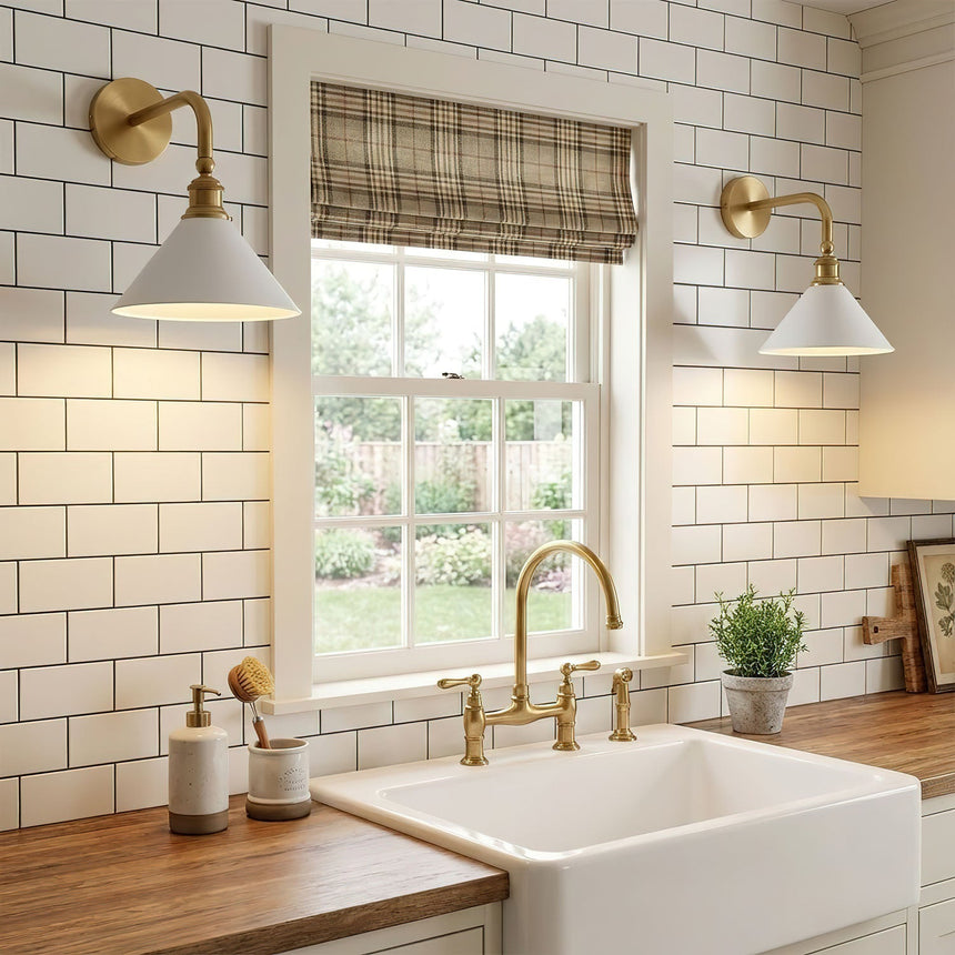 Two sconces lit either side of a window over a white sink and wood counter