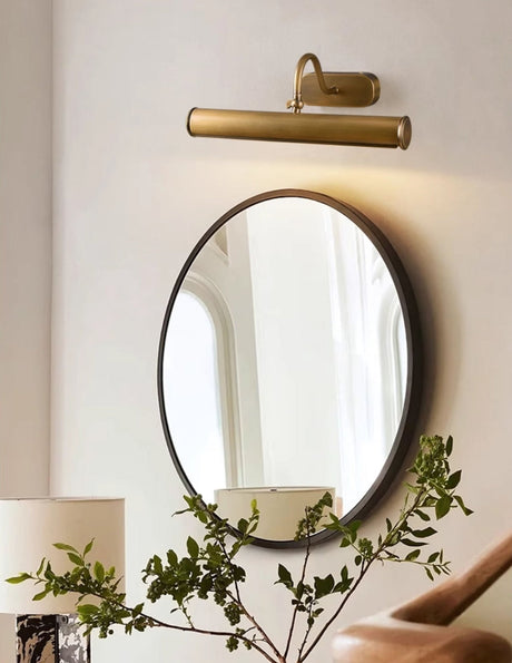 Copper tube lit above a round mirror with trailing foliage beside a lamp