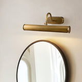 Copper tube lit above a round black framed mirror on a pale wall