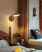 Sconce lit above a bedside table with blossom in a jug beside a spindle bed