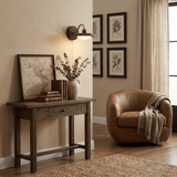 Sconce lit above a console with books beside a leather chair and frames