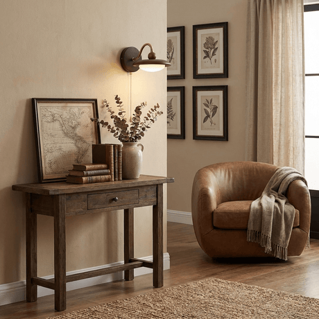 Sconce lit above a console with books beside a leather chair and frames