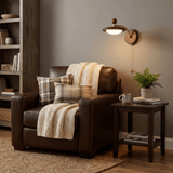 Sconce lit beside a leather armchair with a plaid throw and a plant