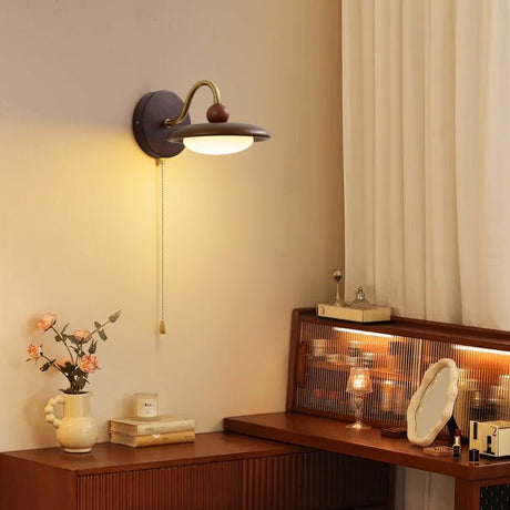Sconce lit above a dresser holding a small mirror and a vase of blossom