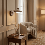 Sconce lit above a side table stacked with books beside a pale armchair