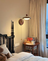 Sconce lit beside a dark spindle bed with a curtain and a bedside jug