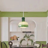 The green glass shade lit above a round table against a green painted wall