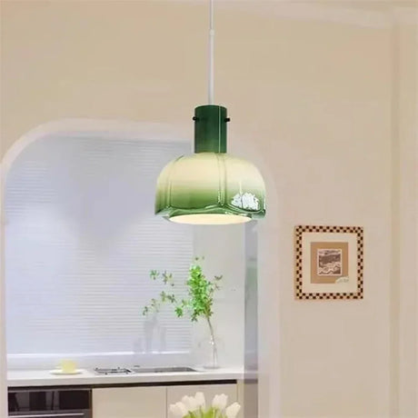 The green glass shade lit above a kitchen counter beside a framed picture