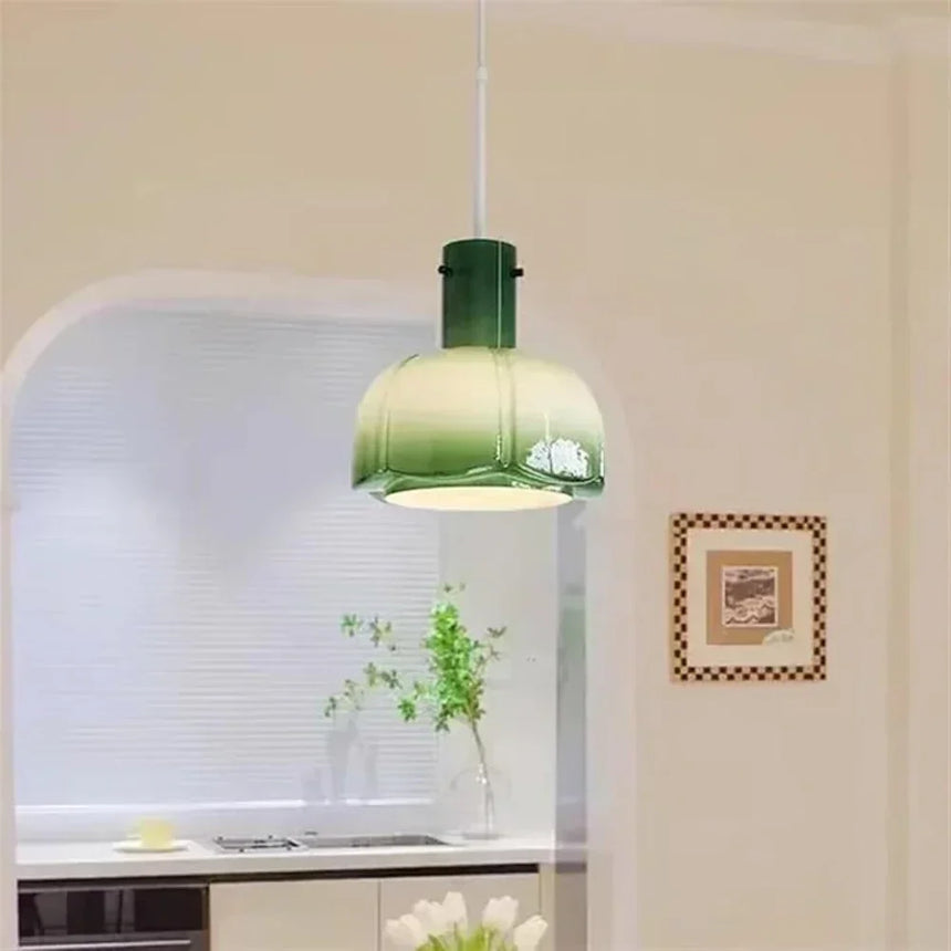 The green glass shade lit above a kitchen counter beside a framed picture