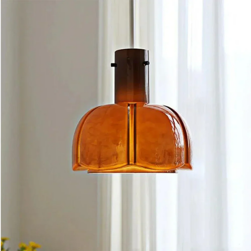 The orange glass shade lit in front of a pale curtain in a bright room