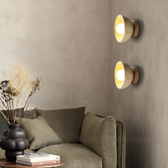 Two sconces lit on a textured wall above a green sofa and a vase of grasses