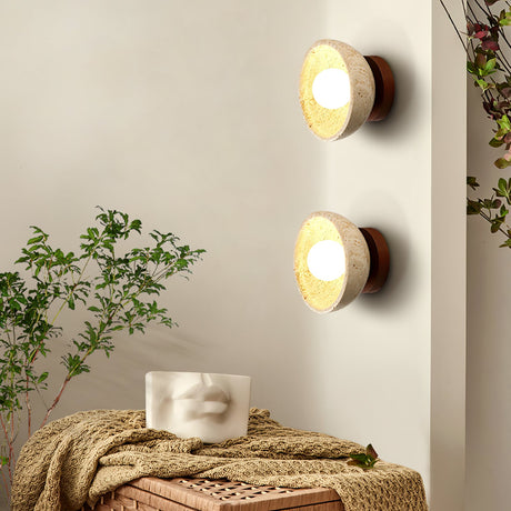 Two sconces lit beside a plant above a bench with a knit throw and a stone