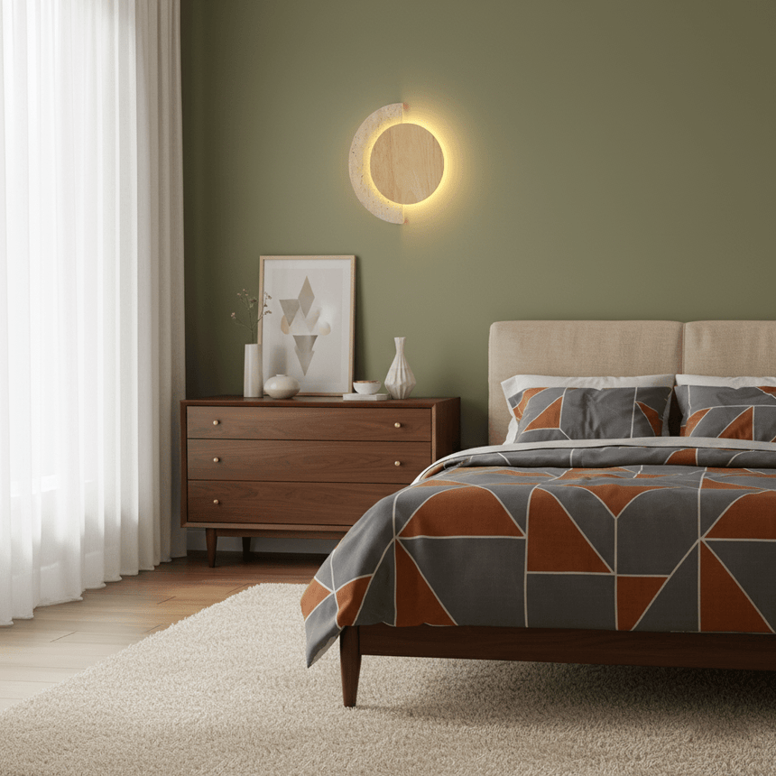 Sconce lit on a deep green wall above a dark wood chest of drawers