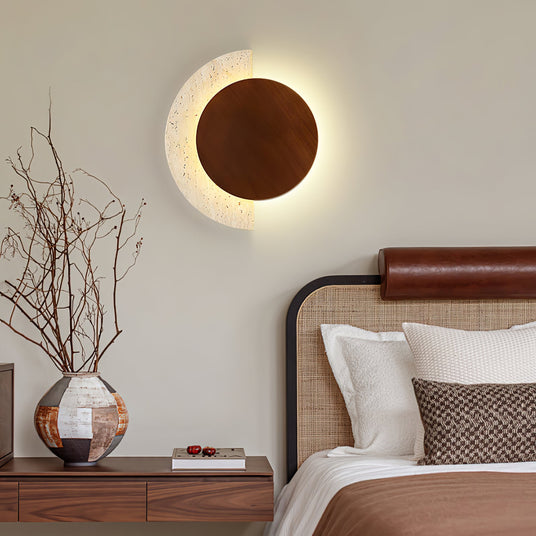 Sconce lit above a nightstand beside a bed with a leather headboard