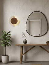 Sconce lit above a console table next to an irregular shaped mirror