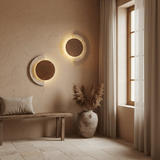 Two sconces of different sizes lit on a plaster wall above a bench