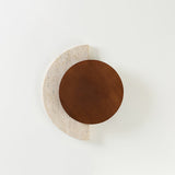 Walnut disc over a travertine crescent unlit, seen straight on