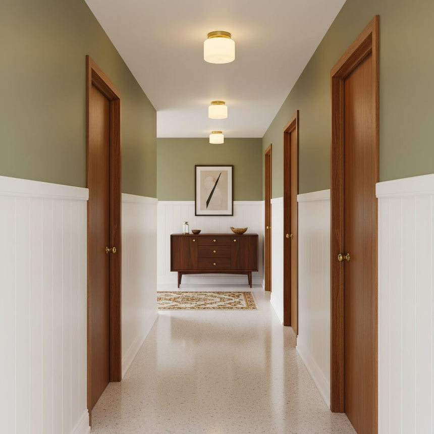 Brass and white glass ceiling lights in a green hallway with a wood sideboard