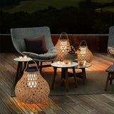 Lanterns lit on small tables on a terrace beside chairs and a lawn