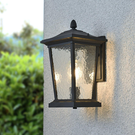 The lantern lit on a gray stucco wall beside a green hedge