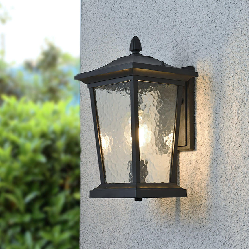 The lantern lit on a gray stucco wall beside a green hedge