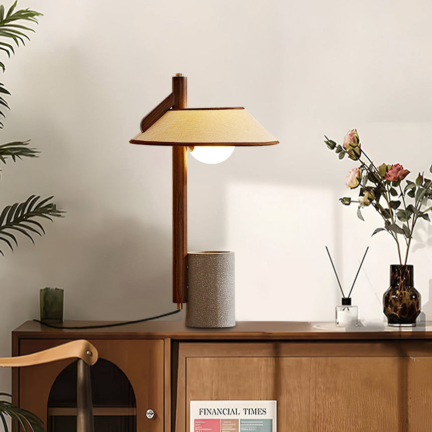 Cement base lamp lit on a sideboard beside a reed diffuser and flowers