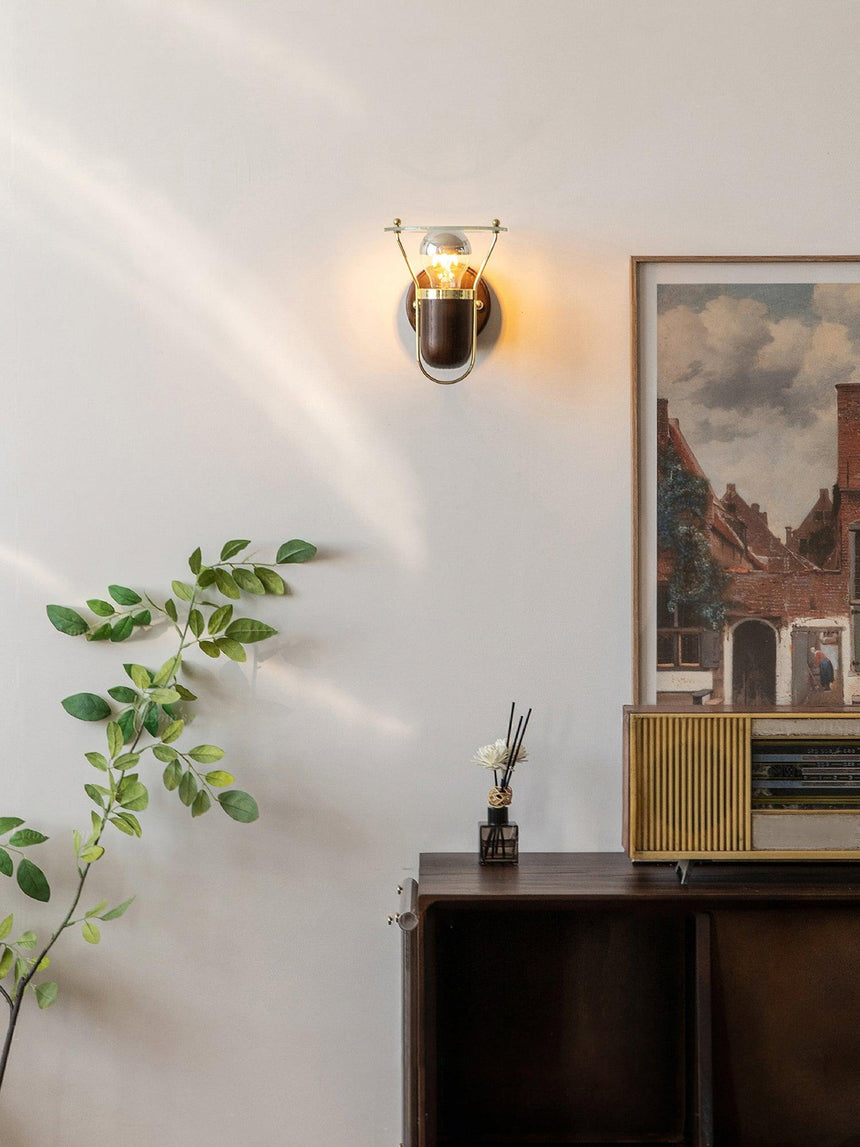 Sconce lit above a sideboard with framed prints, a plant and a small vase