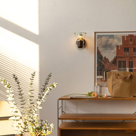Sconce lit beside framed artwork above a shelf unit and dried grasses