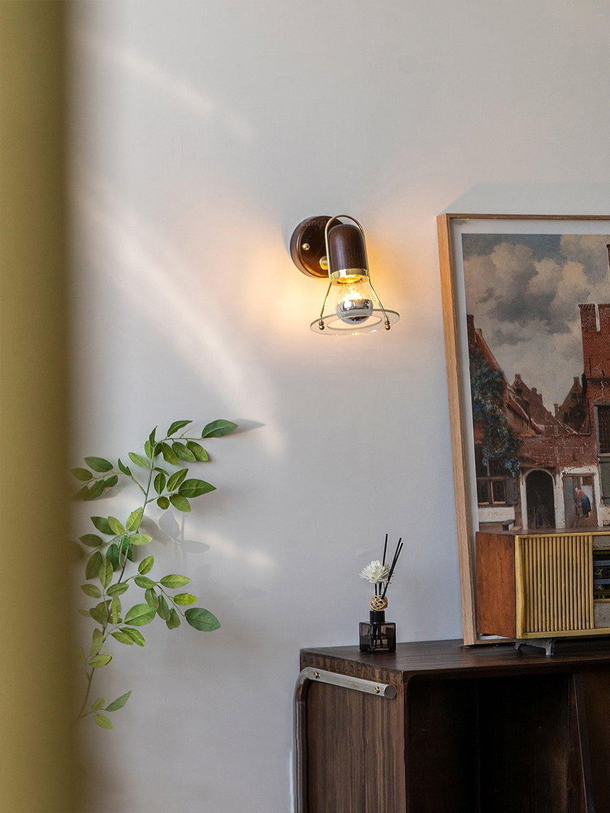 Sconce lit in a room with a plant, framed prints and a dark sideboard