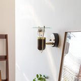 Sconce lit beside a leaning mirror and a plant against a white wall