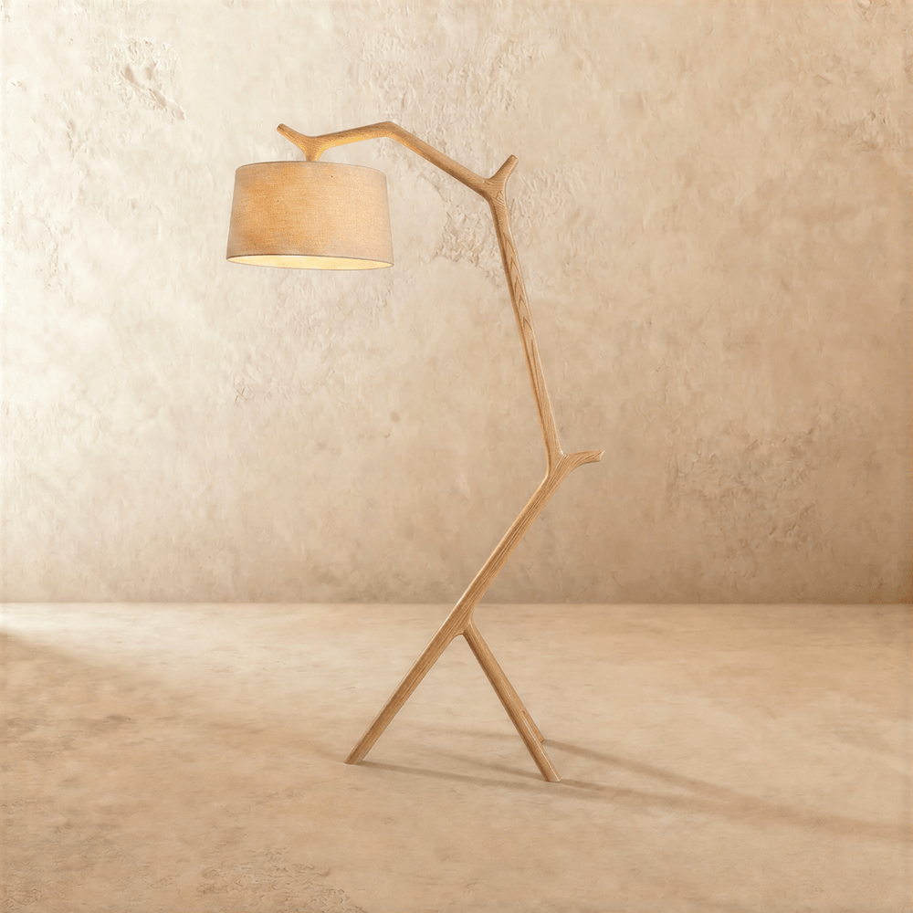 A light wood frame shaped like a branch, leaning forward to carry a cream drum shade