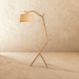 A light wood frame shaped like a branch, leaning forward to carry a cream drum shade