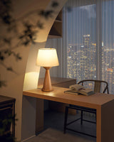 Japandi table lamp lit on a desk in front of a city window at dusk