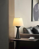 Black based Japandi table lamp lit on a side table beside a dark sofa