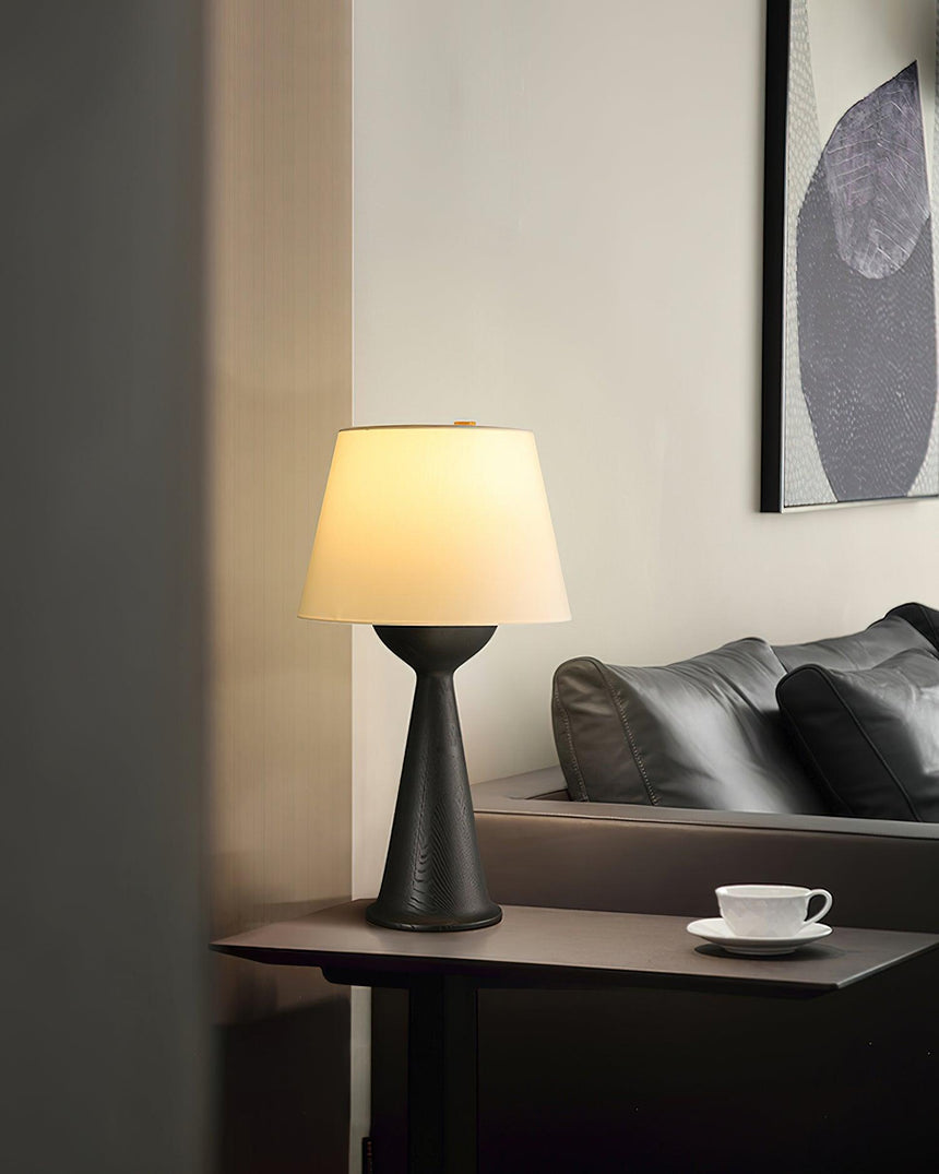 Black based Japandi table lamp lit on a side table beside a dark sofa