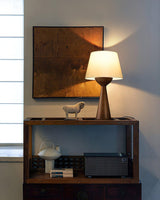 Japandi table lamp lit on a shelf below a framed abstract work