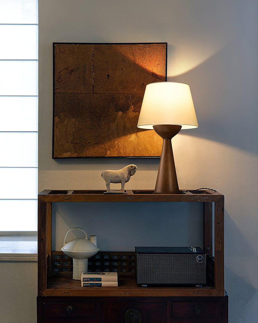 Japandi table lamp lit on a shelf below a framed abstract work