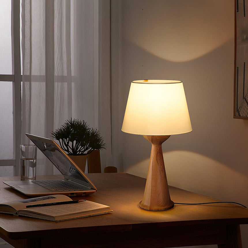 Japandi table lamp lit on a desk beside a laptop and a curtain