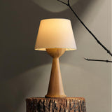 Japandi table lamp lit on a cut tree stump against a warm wall