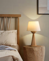 Japandi table lamp lit on a wooden stool beside a bed with a headboard