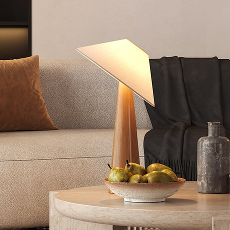 Tilted shade table lamp lit on a round side table beside a pale sofa